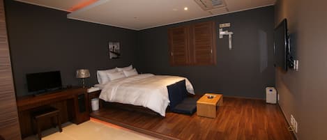 Una habitación de hotel moderna con una cama, un escritorio con televisor, una mesita y un televisor montado en la pared.