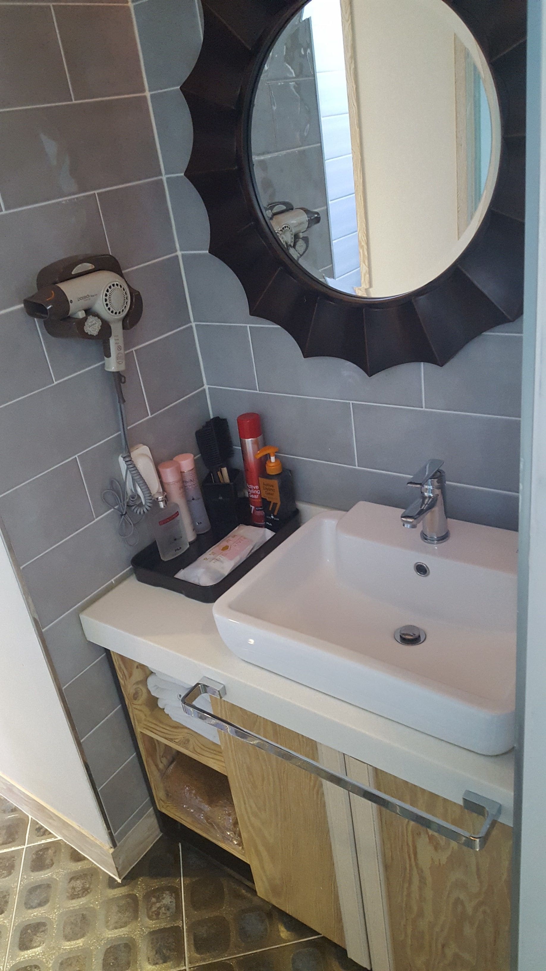Un baño con un lavamanos blanco, un espejo y artículos de tocador sobre la encimera.