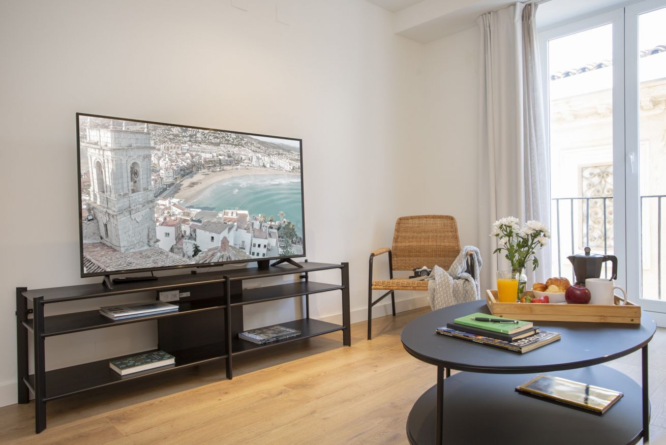 Un soggiorno moderno con una grande TV a schermo piatto, una poltrona in vimini, un tavolino rotondo e un vassoio per la colazione.