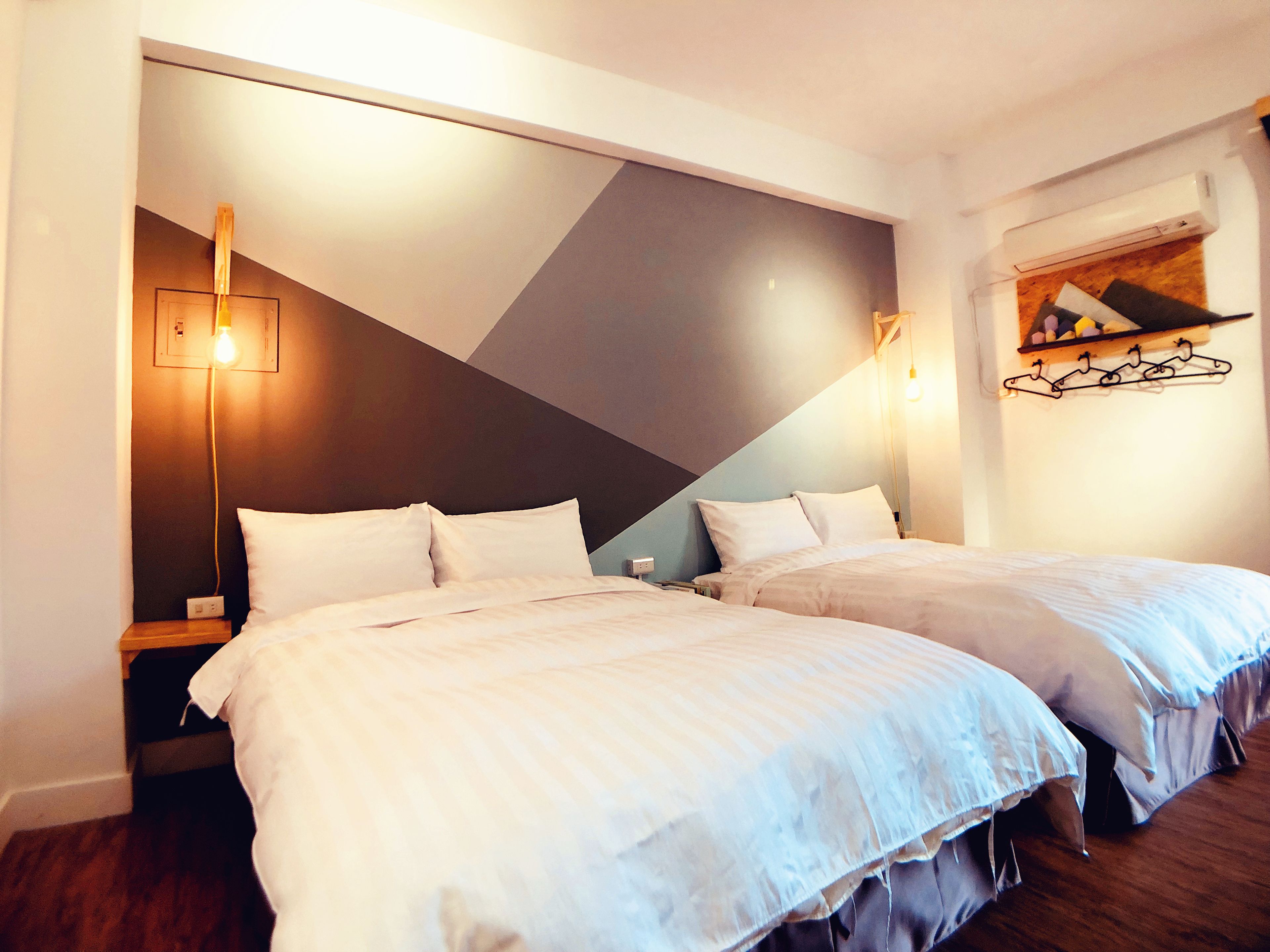 Une chambre d’hôtel avec deux lits, un luminaire moderne et un porte-manteau fixé au mur.