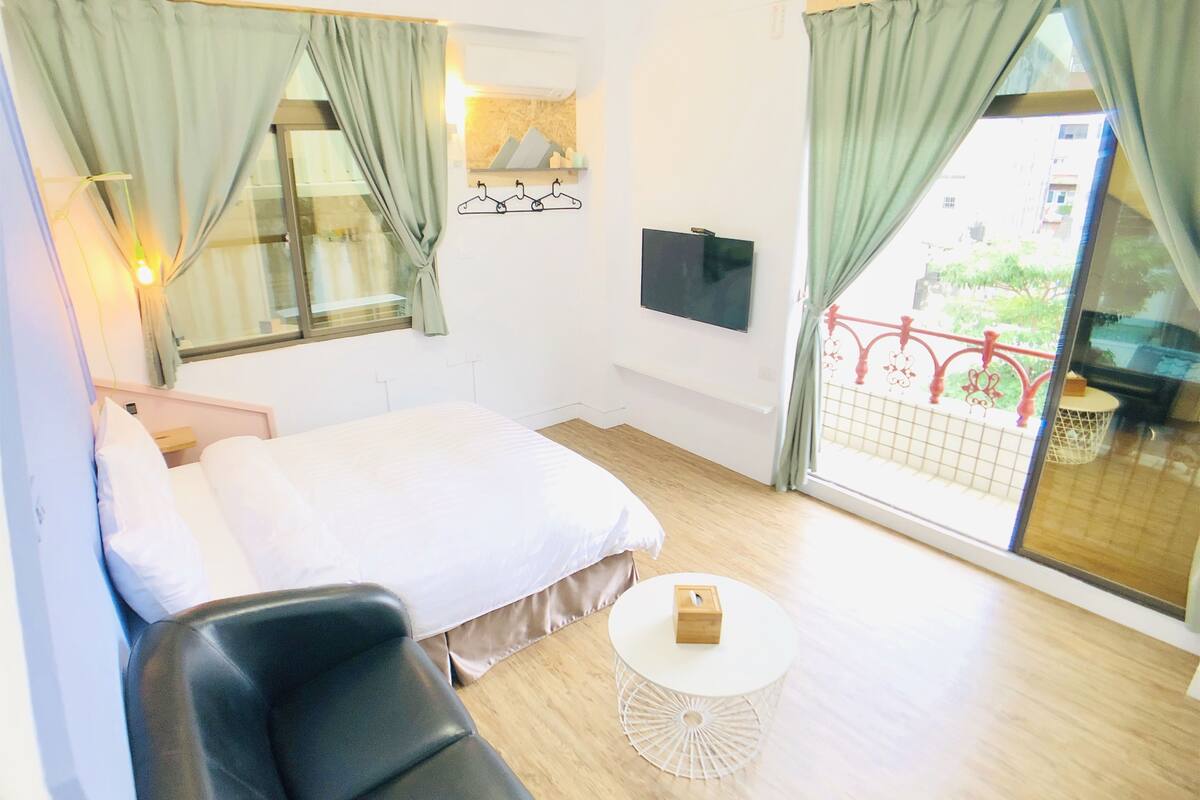 A hotel room with a bed, a chair, a small round table, a TV, and a window with curtains.