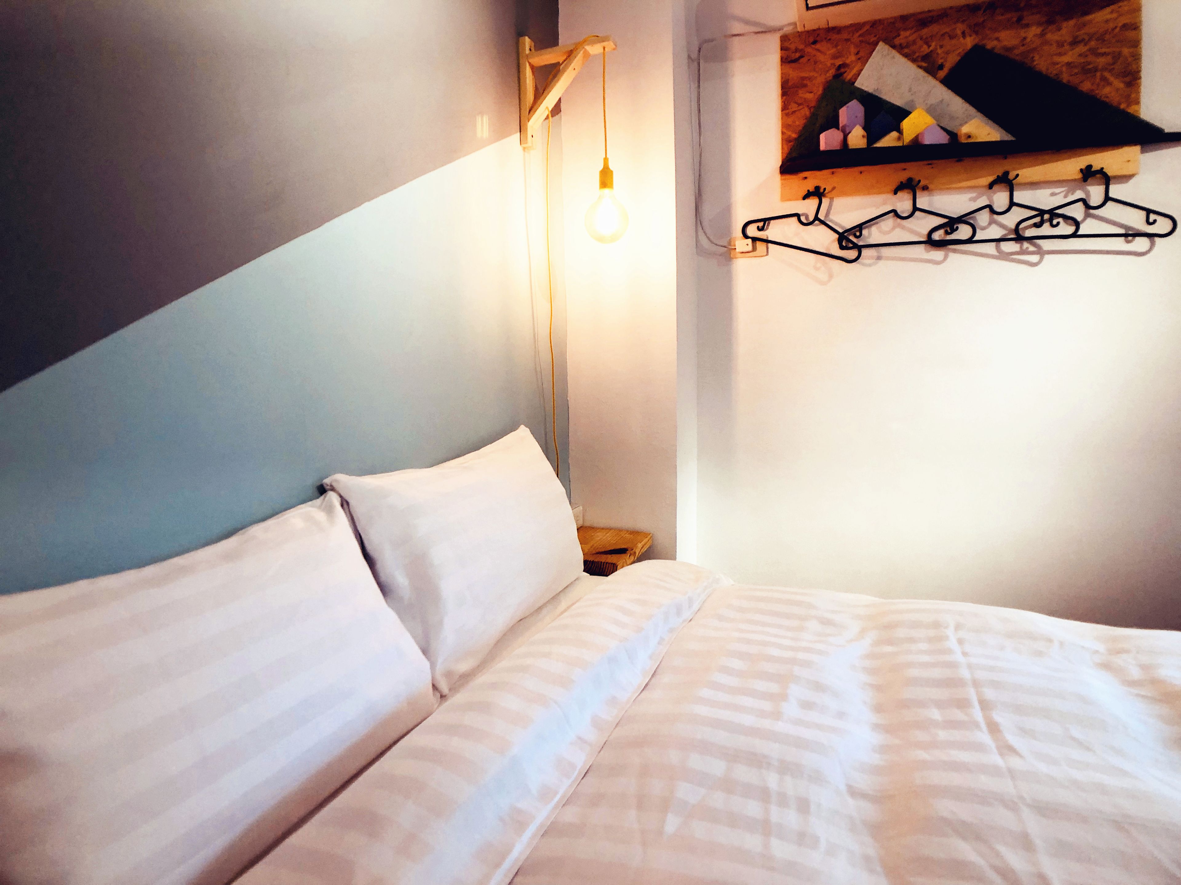 A bedroom with a bed, a hanging light, and a wall-mounted coat rack.