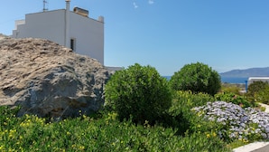 A white building with a flat roof and a chimney, surrounded by greenery and flowers. - villa victor 2 (Naxos)