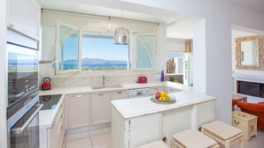 A modern kitchen with a view of the mountains, a dining area with a fireplace, and a cozy seating area. - villa victor 2 (Naxos)