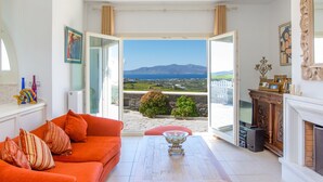 A bright living room with a large window, a red sofa, a coffee table, and a fireplace. - villa victor 2 (Naxos)