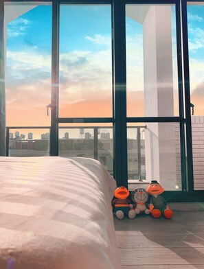 Une chambre avec une grande fenêtre, un lit et deux peluches sur le sol.