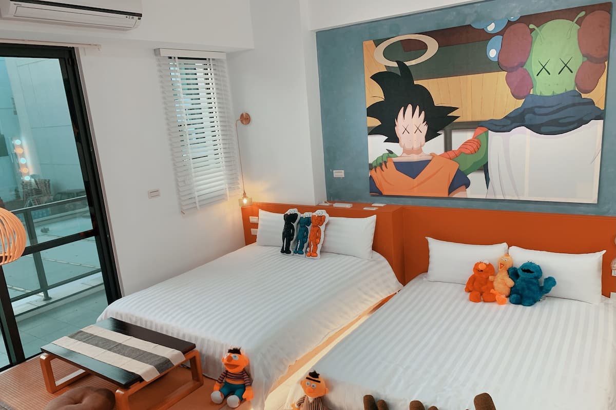 Une chambre d’hôtel avec deux lits, une grande fenêtre, un tableau et des peluches.