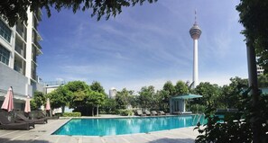 A swimming pool with lounge chairs and umbrellas, surrounded by greenery and a modern building. - Holiday Heaven (Kuala Lumpur)