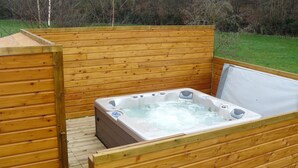 A wooden hot tub with a wooden deck and walls, surrounded by a grassy area. - Comfortable cottage with spa in Mont St Michel Bay (Saint-Martin-Des-Champs)