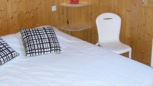 A wooden-paneled room with a bed, pillows, a chair, and a shelf with a red lamp. - Comfortable cottage with spa in Mont St Michel Bay (Saint-Martin-Des-Champs)