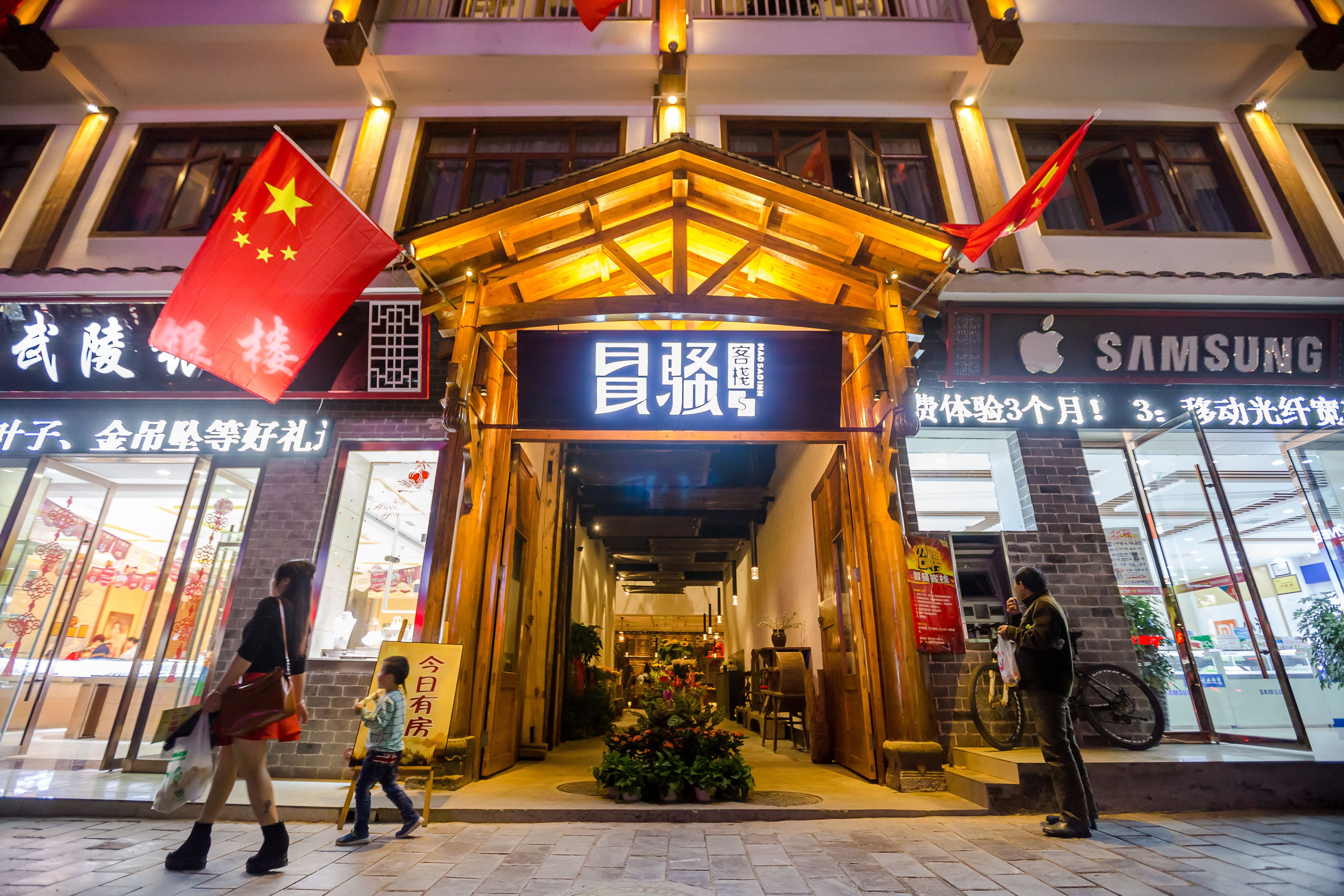 A hotel entrance with a traditional Chinese architectural design, featuring a wooden pavilion and red flags.