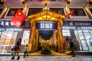 A hotel entrance with a traditional Chinese architectural design, featuring a wooden pavilion and red flags.