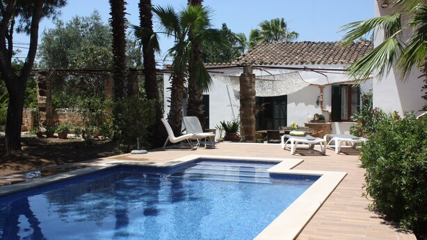 A rectangular swimming pool with tiled edges, surrounded by a wooden deck. There are lounge chairs and a small table with a canopy. - House ideal for families with children, large garden with pool and playground (Can Picafort)