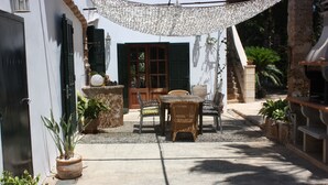 An outdoor patio area with a table and chairs, potted plants, and a grill. - House ideal for families with children, large garden with pool and playground (Can Picafort)