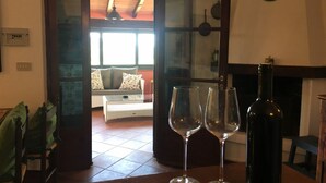 An open door leading to a living room with a sofa and a fireplace. Two wine glasses and a bottle are on a table in the foreground.