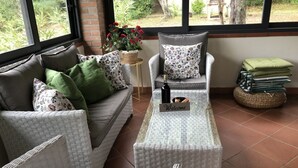 A cozy seating area with wicker furniture, a 'Welcome' sign, and a view of greenery outside.
