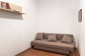 A corner room with a beige sofa, a small bookshelf, and a framed picture on the wall.