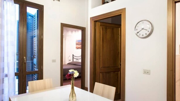 A dining area with a white table, a vase with flowers, wooden doors, and a wall clock. - Oriuolo Palace Fantastic, brand-new apartment in the heart of Florence (Florence)