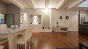 Una cocina moderna con horno empotrado, un comedor con mesa y sillas blancas, y suelo de madera.