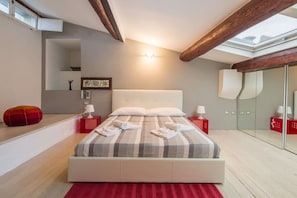Ein modernes Schlafzimmer mit einem großen Bett, einem Oberlicht, einem roten Hocker und einem roten Nachttisch mit einer Lampe.