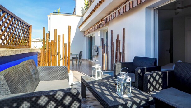 An outdoor seating area with wicker furniture, a table with a lantern, and a view of a building with a tiled roof and a wooden fence. - Amazing Terrace in the Center by Hello Homes Sitges (Sitges)