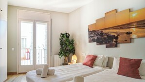 A hotel room with two beds, a balcony, a plant, and a sunset painting on the wall. - Amazing Terrace in the Center by Hello Homes Sitges (Sitges)