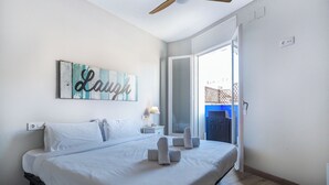 A bedroom with a bed, a ceiling fan, a wall-mounted artwork with the word "Laugh", and a view through an open door. - Amazing Terrace in the Center by Hello Homes Sitges (Sitges)