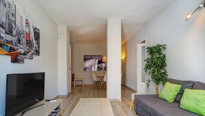 A modern living room with a flat-screen TV, a coffee table, a sofa with green cushions, a bookshelf, and a wall-mounted plant. - Amazing Terrace in the Center by Hello Homes Sitges (Sitges)