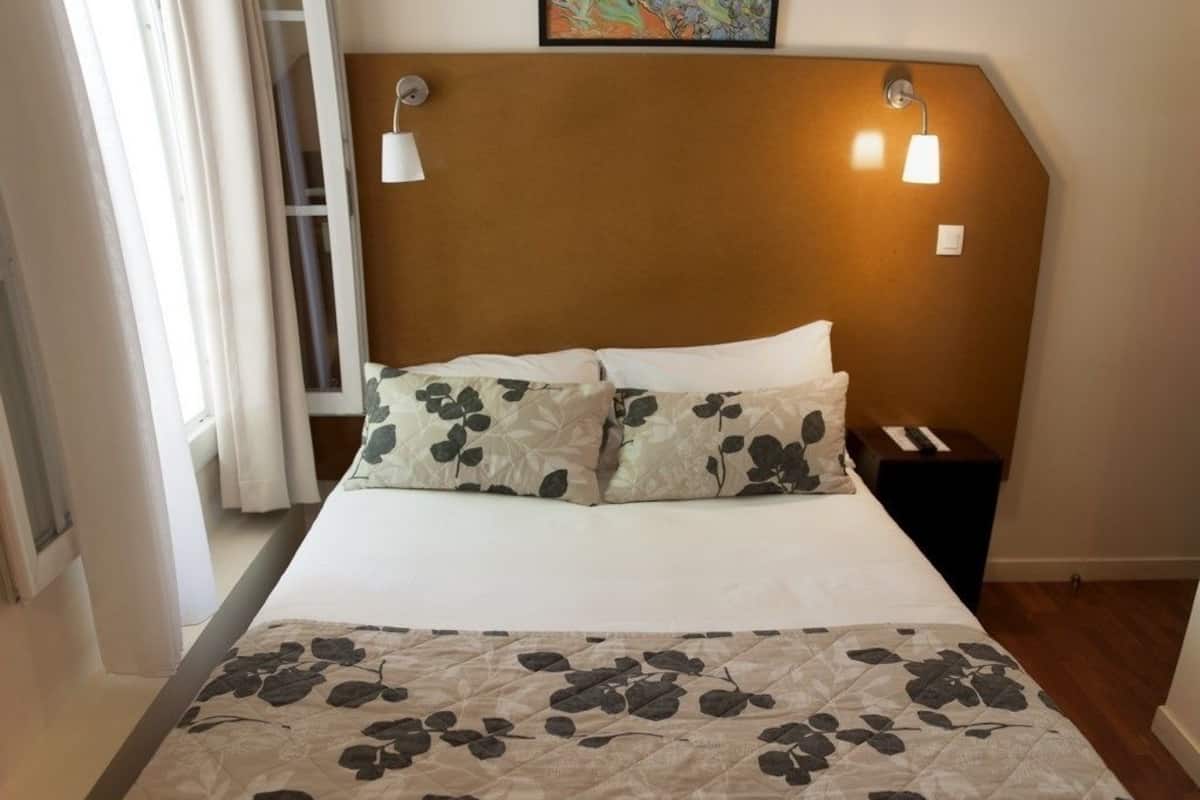 A neatly made bed with floral-patterned pillows and a quilt, a bedside table with a lamp, and a painting above the bed.