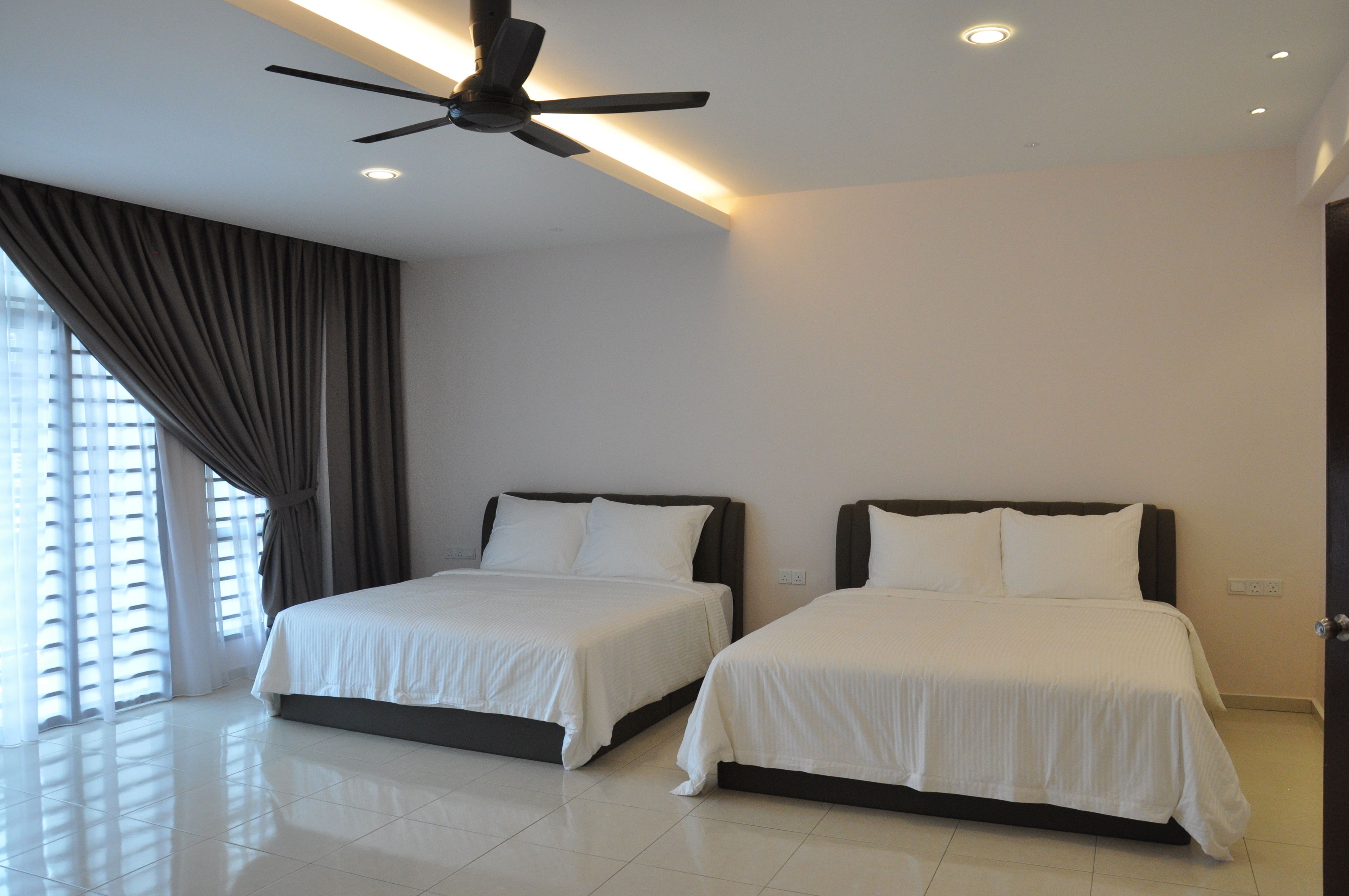 Habitación de hotel con dos camas, ventilador de techo y un amplio ventanal con cortinas.