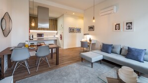 A modern living room with a sofa, a dining table with chairs, and a kitchen in the background.