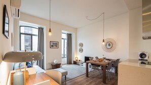 A modern living room with a wooden floor, a dining area with a table and chairs, and a kitchen area with a stove and a microwave.