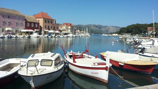 A marina with boats docked, buildings with red roofs, and a clear blue sky. - Maslina Tree House (Hvar) - Peaceful retreat with garden & close to the sea (Stari Grad)