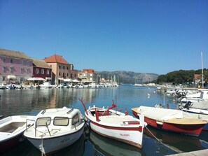 A marina with boats docked, buildings with red roofs, and a clear blue sky. - Maslina Tree House (Hvar) - Peaceful retreat with garden & close to the sea (Stari Grad)