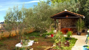A stone building with a tiled roof, surrounded by a garden with various plants and a wooden fence. - Maslina Tree House (Hvar) - Peaceful retreat with garden & close to the sea (Stari Grad)