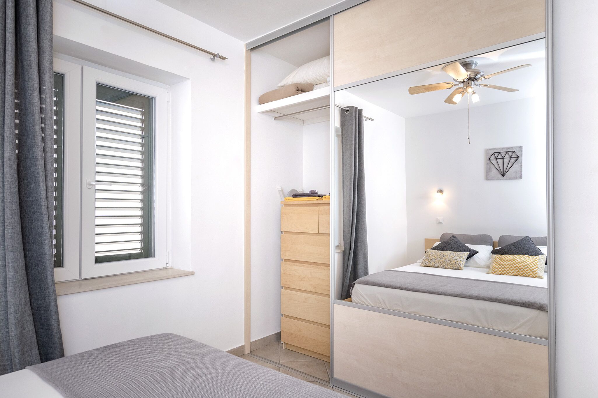 A modern bedroom with a bed, a wardrobe, a mirror, and a ceiling fan.