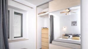 A modern bedroom with a bed, a wardrobe, a mirror, and a ceiling fan. - Maslina Tree House (Hvar) - Peaceful retreat with garden & close to the sea (Stari Grad)