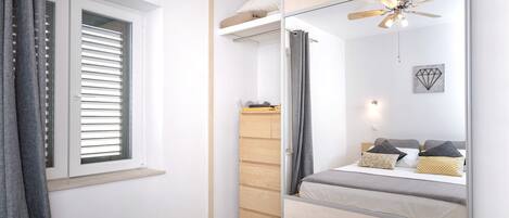 A modern bedroom with a bed, a wardrobe, a mirror, and a ceiling fan.