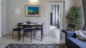 Un comedor con una mesa preparada para cuatro, un cuadro en la pared, una planta y un sofá en la sala de estar.