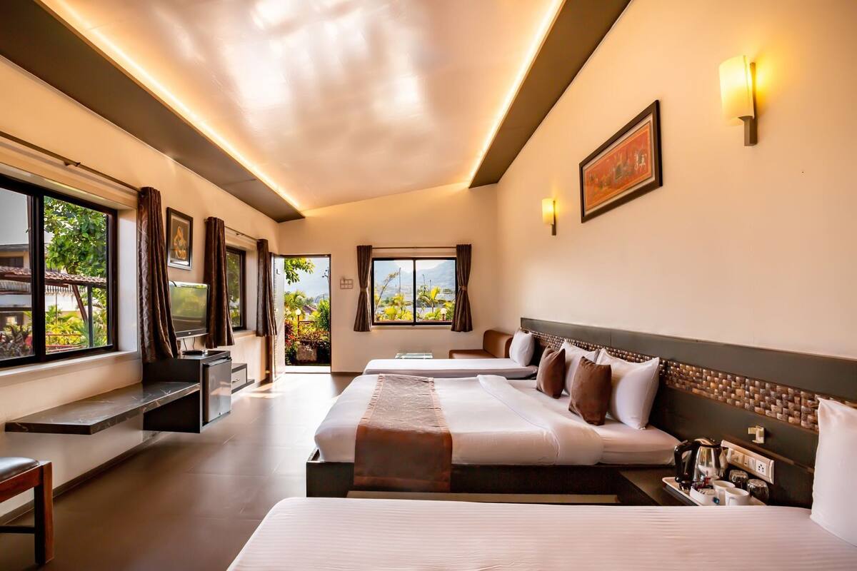 Habitación de hotel con dos camas, un escritorio, televisión y vistas al exterior con zonas verdes.