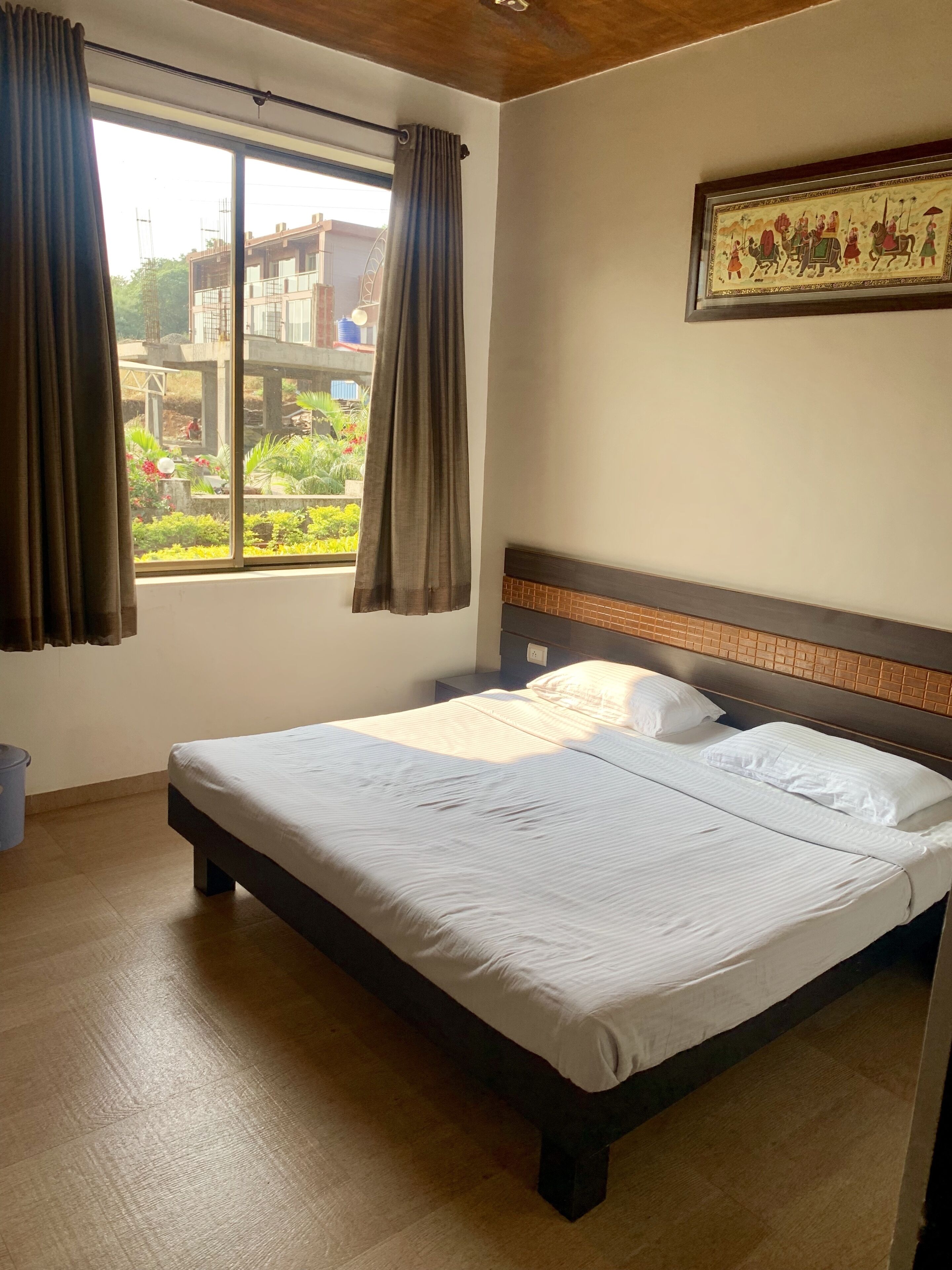 Habitación de hotel con una cama grande, ventana con cortinas, un cuadro en la pared y vistas al jardín exterior.