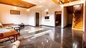 En rummelig opholdsstue med trælofter, en lysekrone, en sofa, et sofabord og et fjernsyn ophængt på væggen.