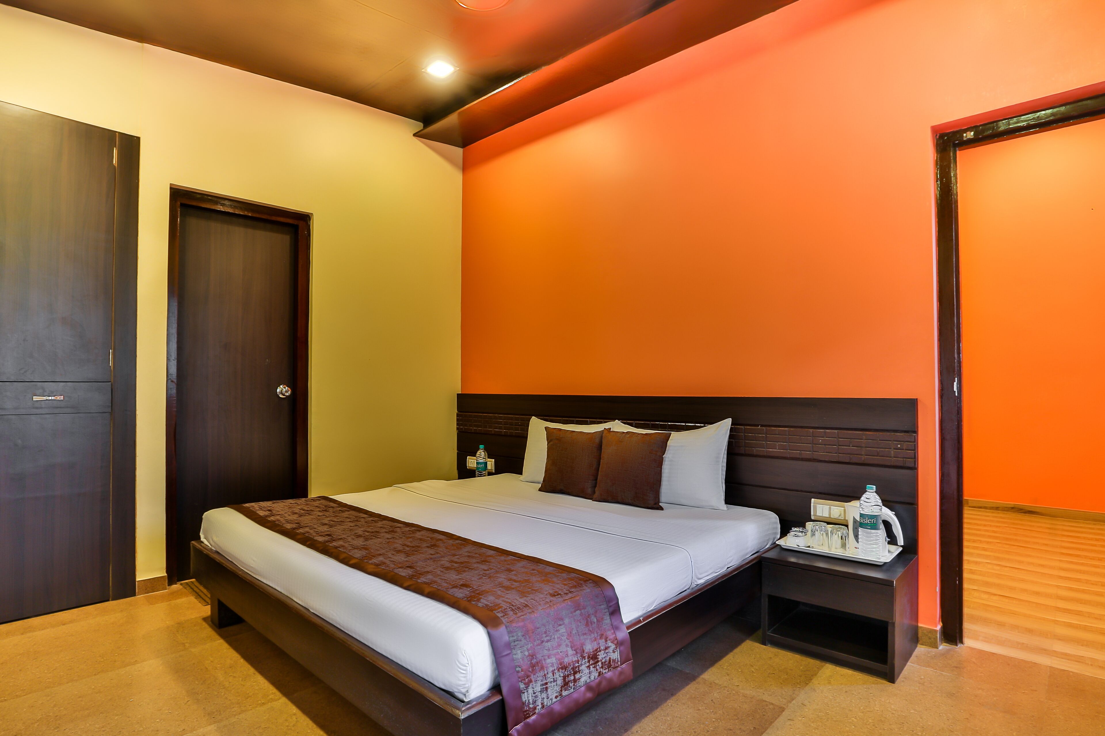 A hotel room with a bed, a nightstand, a water bottle, and a tray with glasses and a bottle.