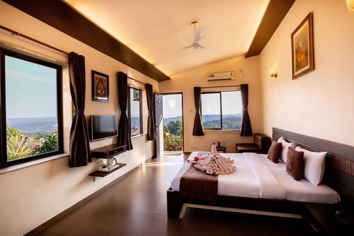 Habitación de hotel con cama, televisión y ventanas amplias que ofrecen vistas al paisaje.