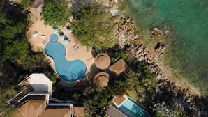 An aerial view of a resort with a large swimming pool, beach area, and multiple lounge chairs. - The Bay Samui (Koh Samui)