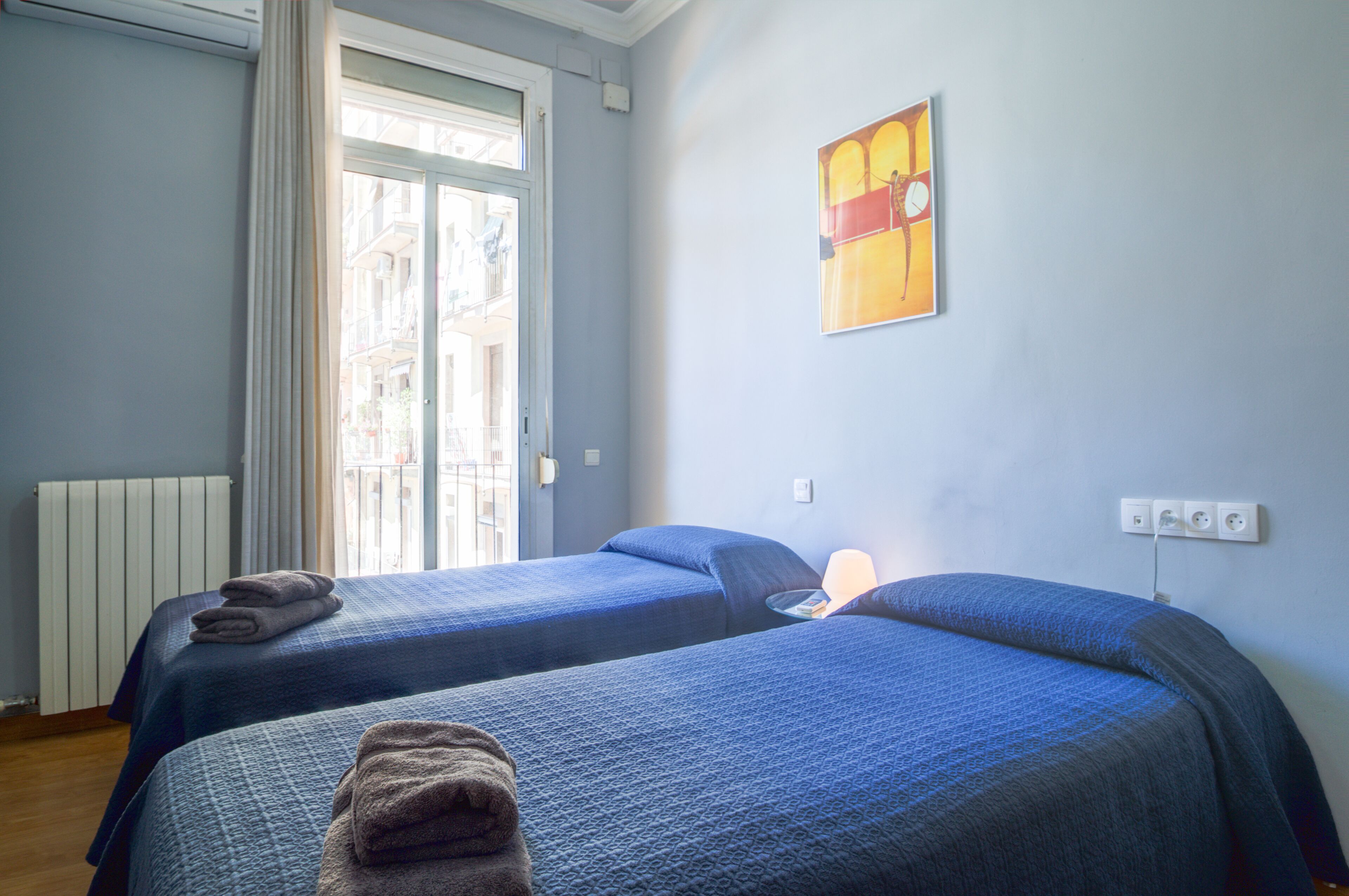 Een hotelkamer met twee bedden, een radiator, een raam met gordijnen en een schilderij aan de muur.