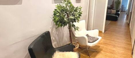A modern hallway with a black leather chair, a white chair, and a potted plant.