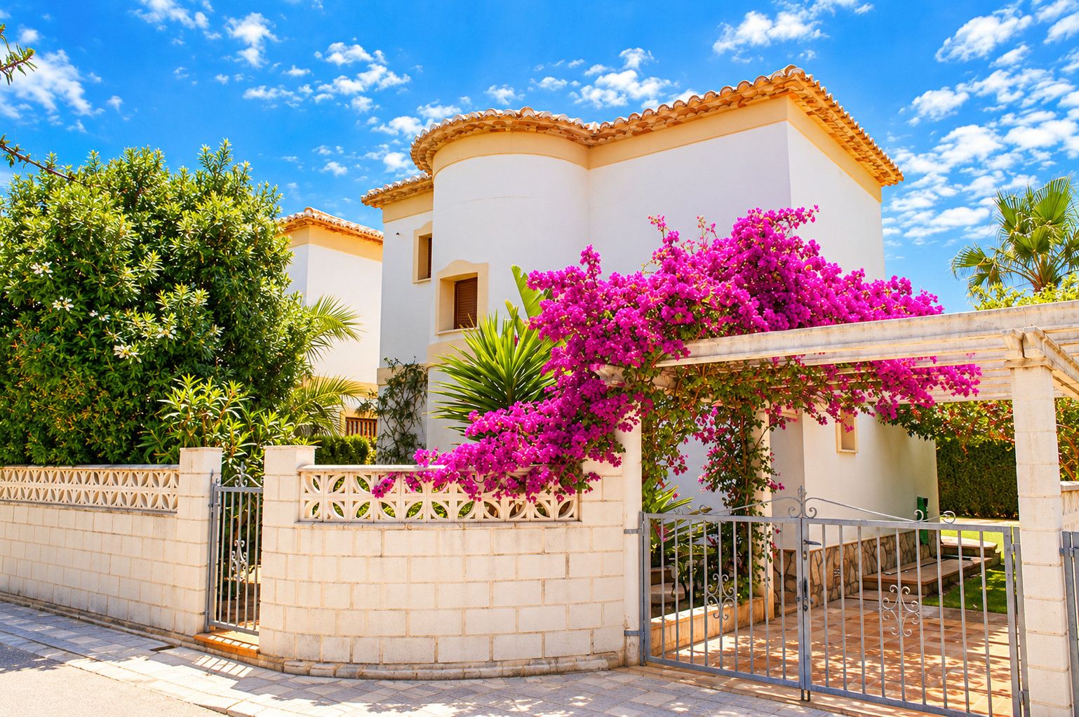 A white building with a curved roof, a gated entrance, and vibrant pink bougainvillea flowers.
