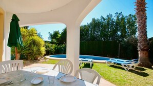 Une terrasse extérieure avec une table dressée pour les repas, une piscine et des chaises longues.