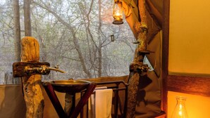 Een rustiek interieur met een houten tafel, een hanglamp en uitzicht op bomen door een raam.